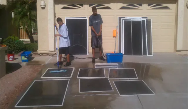 Two workers washing window screens laid flat on a wet driveway