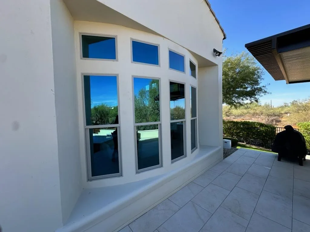 A white stucco wall with a curved run of windows beside a covered patio